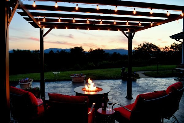 Comfortable outside seating area with fire pit table and a pergola with lights in the evening